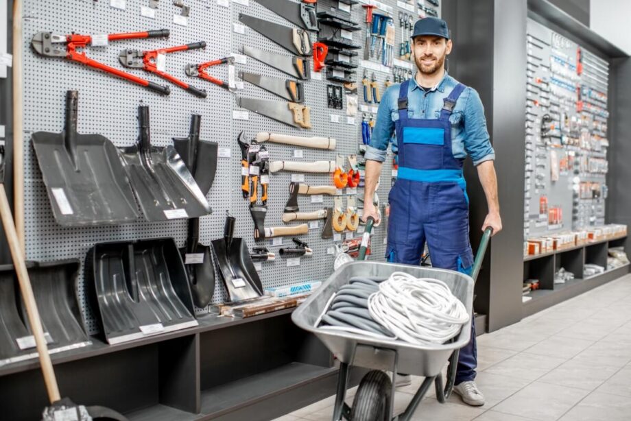 Mężczyzna w sklepie z materiałami budowlanymi pcha taczkę pełną kabli.