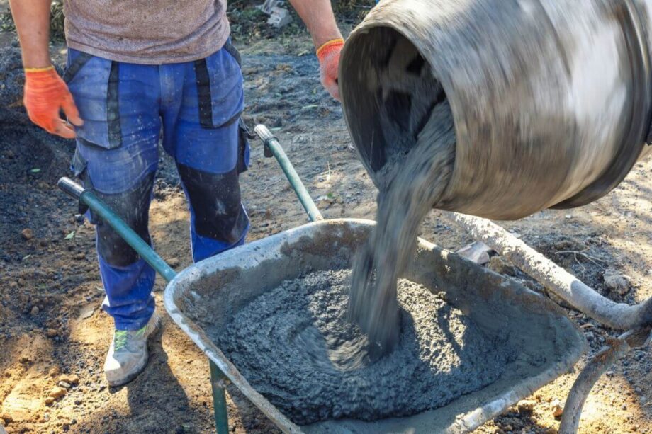 Mężczyzna wylewa beton z betoniarki do taczki.
