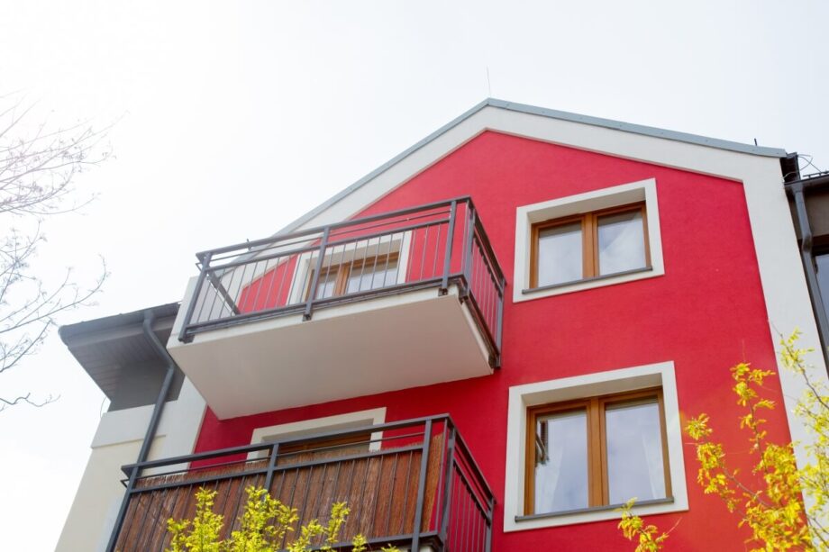 Czerwone elewacje budynku z widocznym balkonem i oknami.